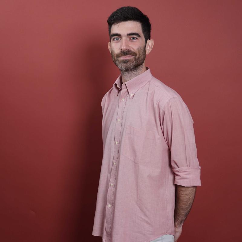 Francesco Zaffarano stands in front of a deep red background in a half profile with his arms crossed behind his back.